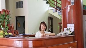 A reception desk with a wooden finish, a telephone, and a small plant. - Phong Lan Guesthouse (Hue)