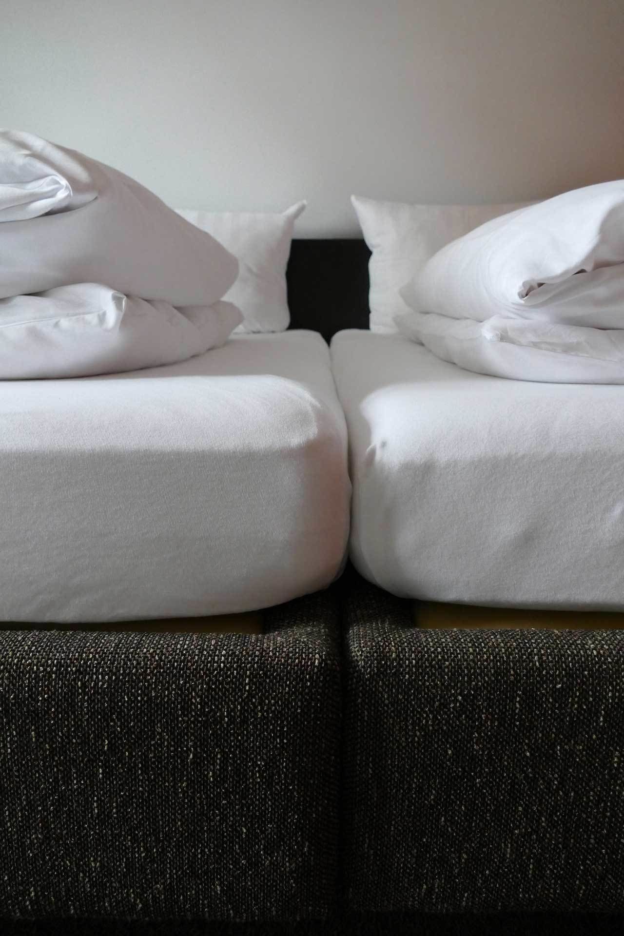 Una cama doble con ropa blanca y un sofá oscuro y texturizado al frente.