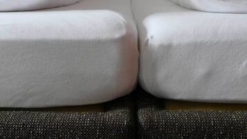Una cama doble con ropa blanca y un sofá oscuro y texturizado al frente.