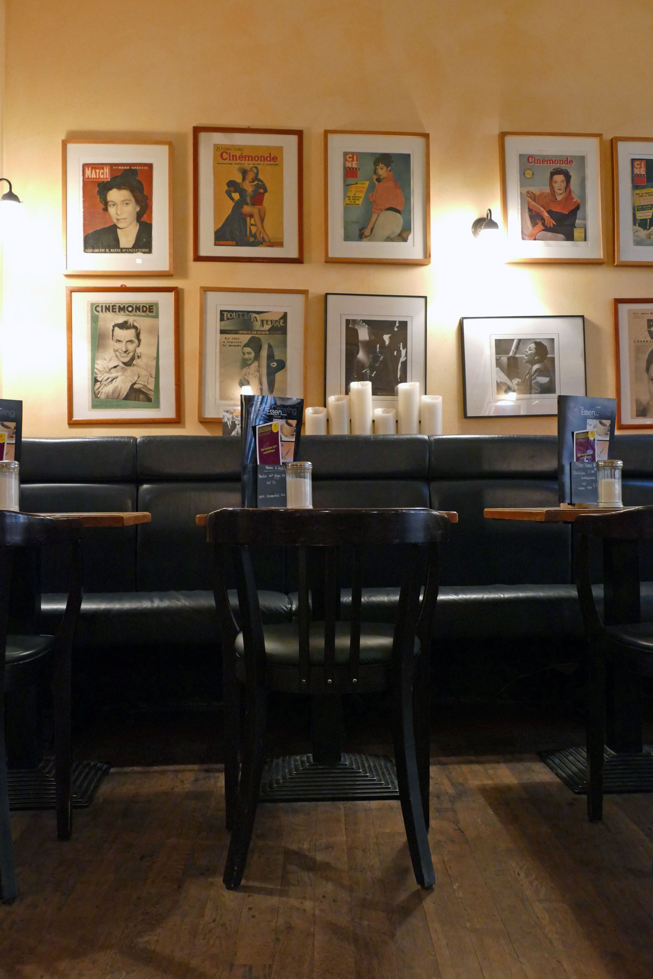 Interior de restaurante com assentos de couro preto, mesas de madeira e cartazes emoldurados na parede.
