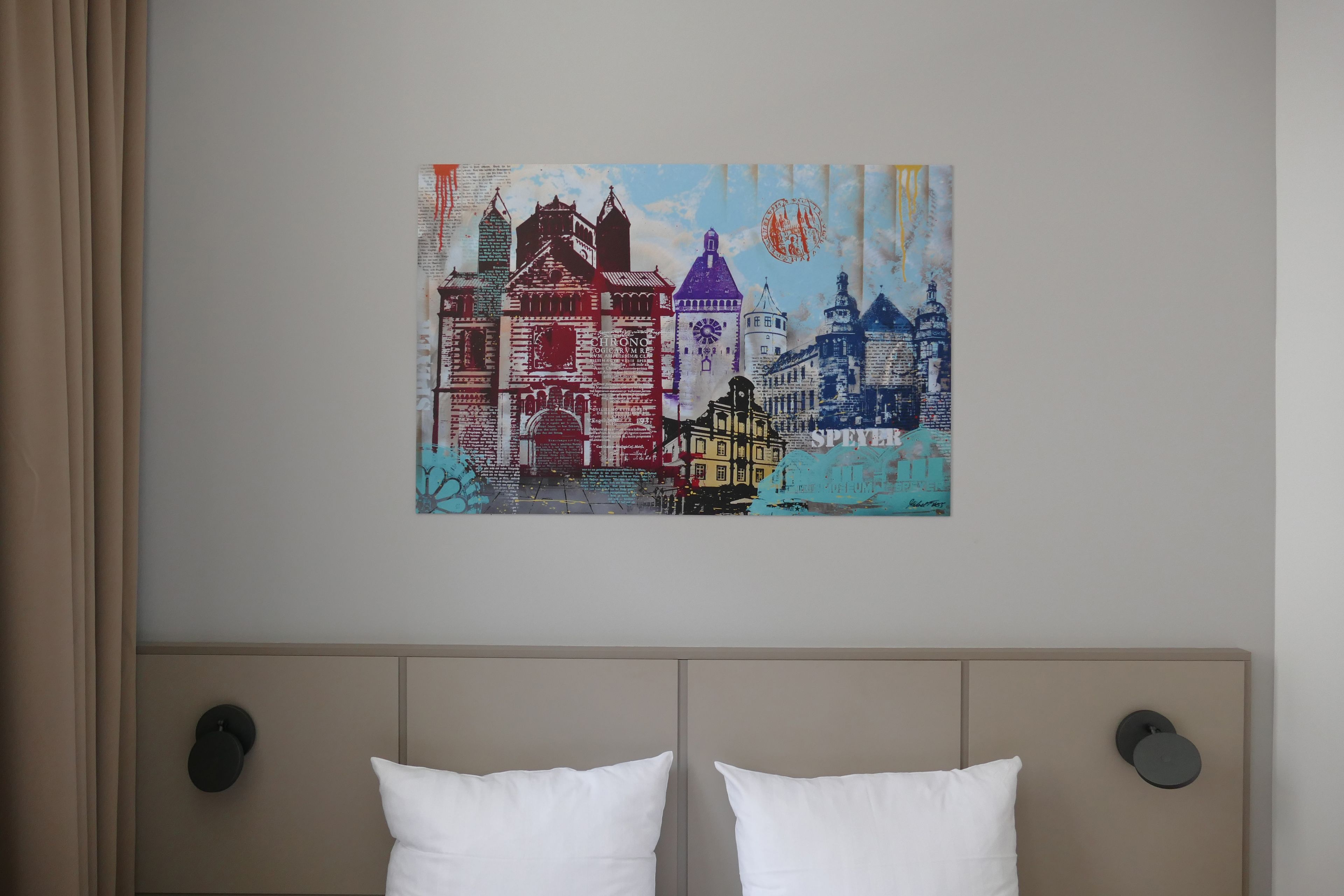 Ein Schlafzimmer mit einem Bett, zwei Kissen und einem Wandbild mit bunten Gebäuden.