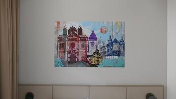 Ein Schlafzimmer mit einem Bett, zwei Kissen und einem Wandbild mit bunten Gebäuden.