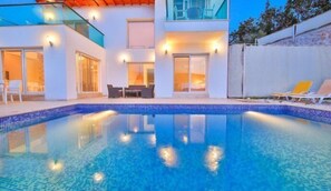 Ett modernt hus med en swimmingpool, utomhusmöbler och ett glasräcke.