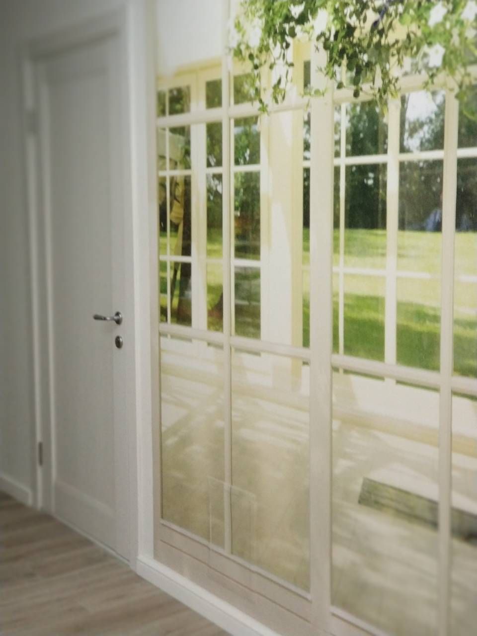 A room with a large window, a door, and a wooden floor.