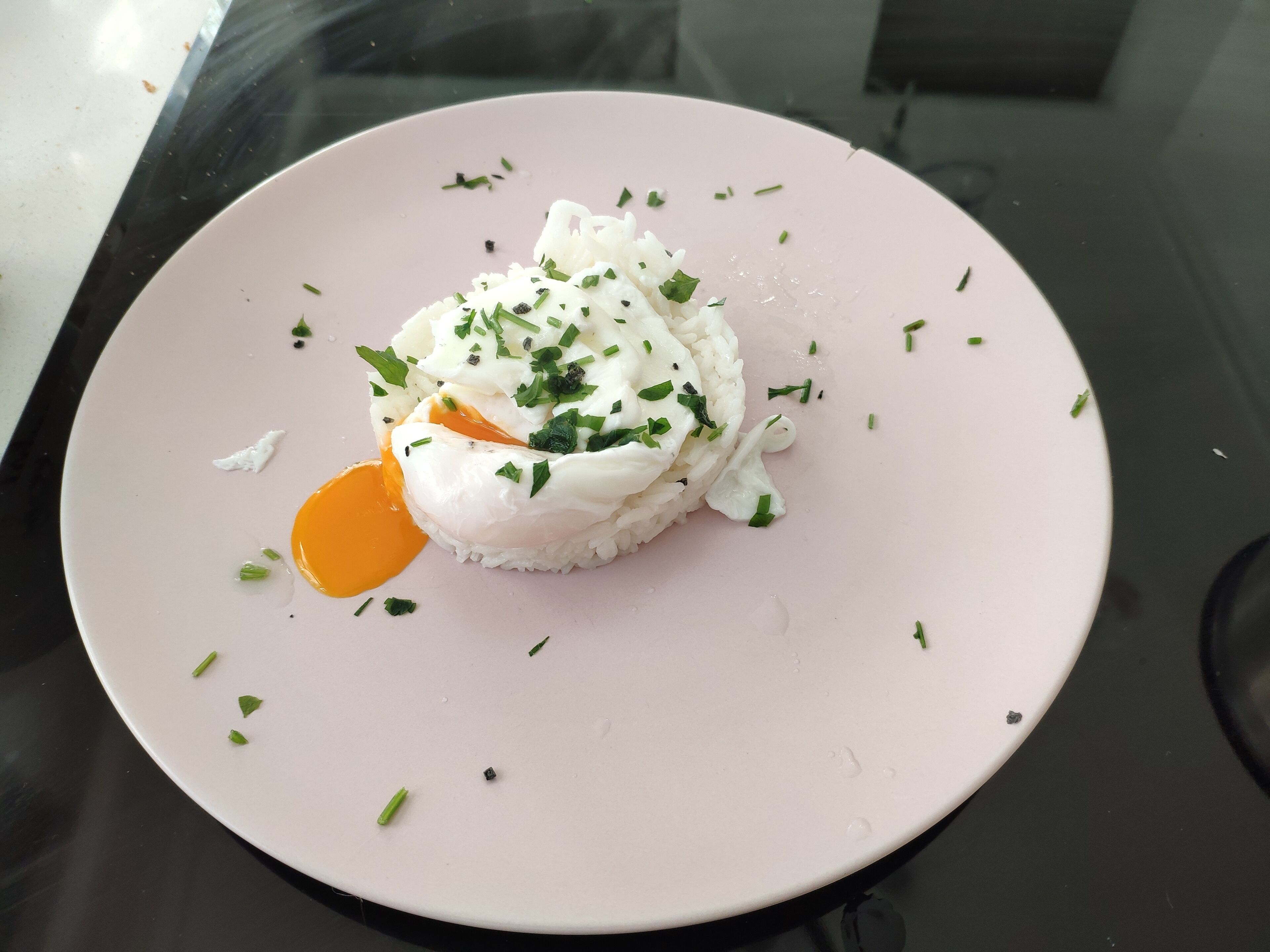 A plate with a poached egg on top of rice, garnished with chives.