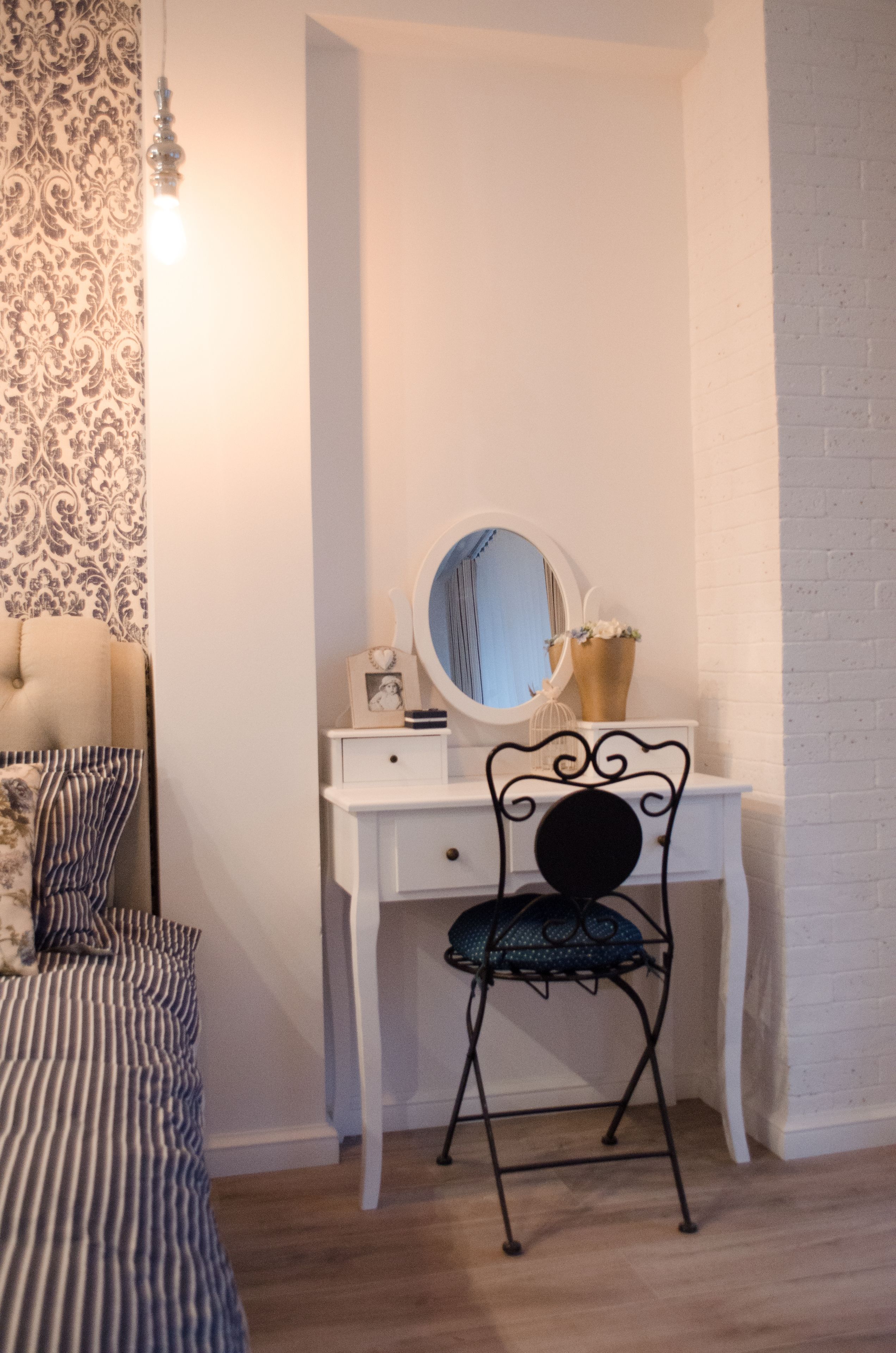 A bedroom with a bed, a dresser, a chair, a mirror, and a wall with patterned wallpaper.