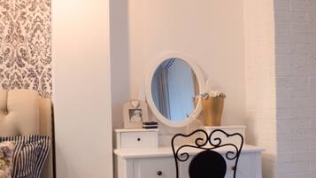 A bedroom with a bed, a dresser, a chair, a mirror, and a wall with patterned wallpaper.