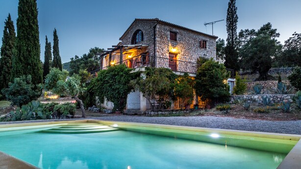 Una casa de piedra con piscina, rodeada de follaje y árboles.