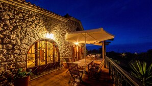 Un edificio de piedra con un patio que incluye una mesa, sillas, un parasol grande y una planta en maceta.