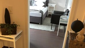 Un pasillo que conduce a un dormitorio con cama, mesita de noche, lámpara y una peque ña mesa con una cesta.