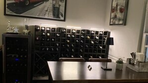 Un comedor con una mesa, sillas, una estantería para vinos y un refrigerador.