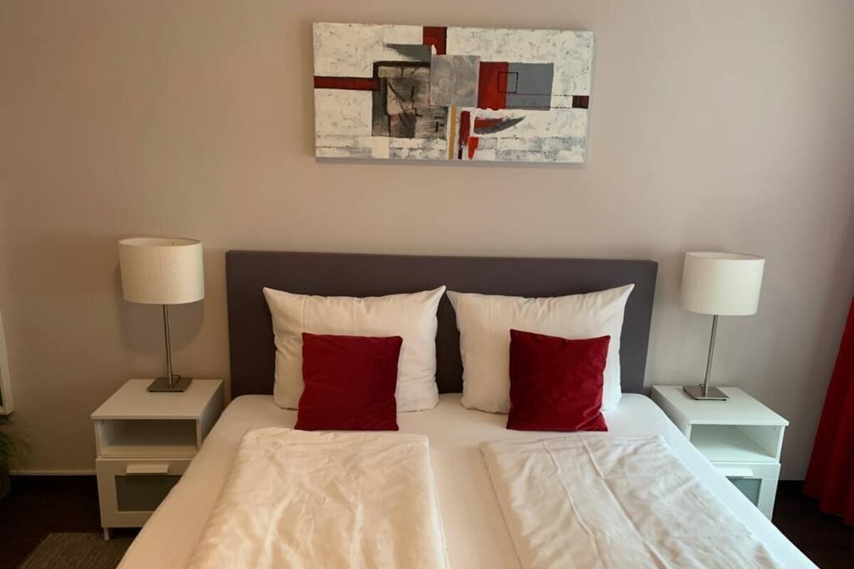 Ett hotellrum med en stor säng, två sängbord med lampor, en röd och vit abstrakt målning på väggen och en röd gardin.