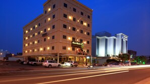 Un hotel de varios pisos con una entrada destacada y un estacionamiento al frente.