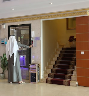 A hotel lobby with a reception desk, a digital phone, a staircase, and a potted plant. - Park Jizan Hotel (Jizan)