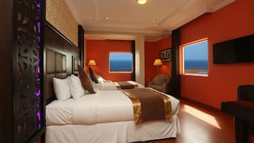 A hotel room with a large bed, two windows with ocean views, a television, and a decorative wall panel.