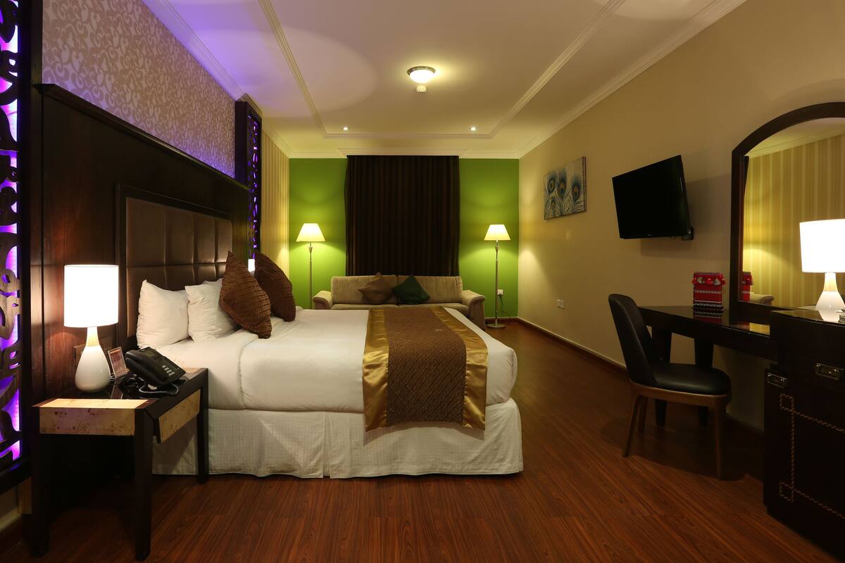 A hotel room with a large bed, bedside lamps, a desk with a chair, and a television.