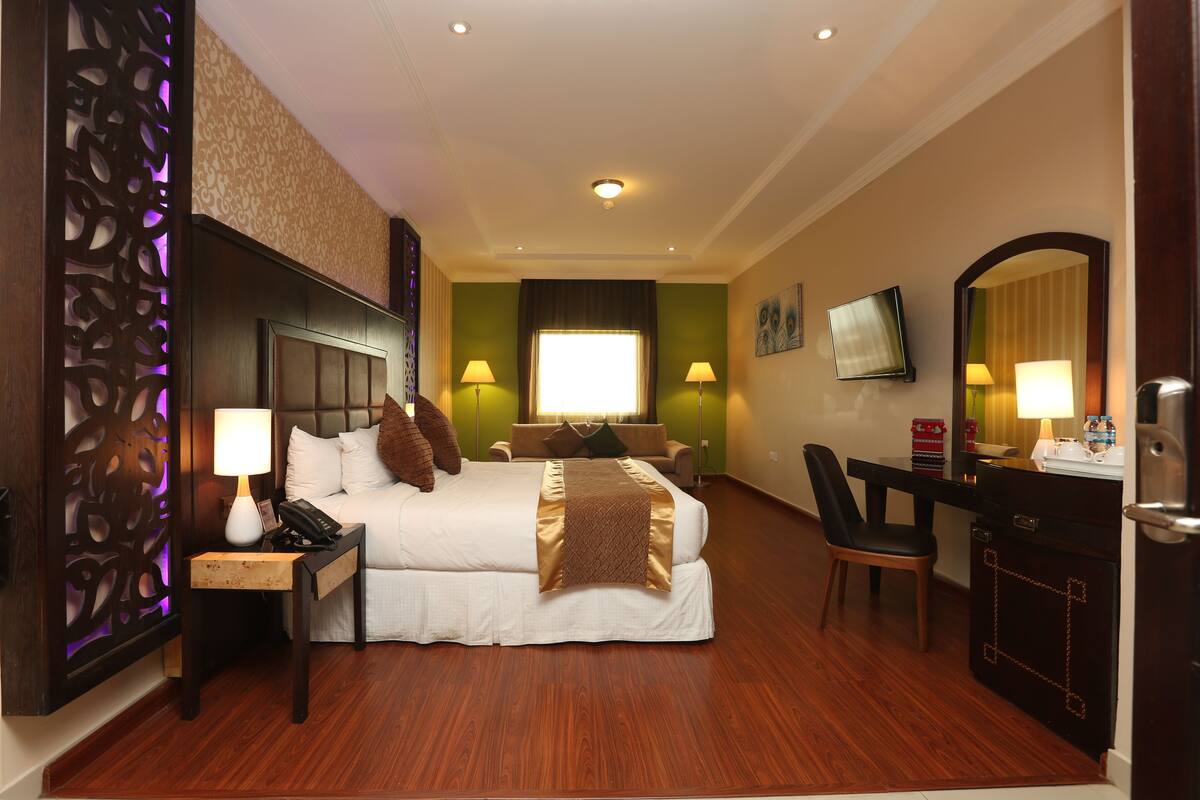 A hotel room with a bed, bedside lamps, a desk with a chair, a television, and a mirror.