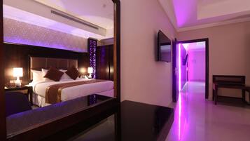 Habitación de hotel con una cama grande, mesitas de noche, un televisor montado en la pared y un espejo que refleja la habitación.