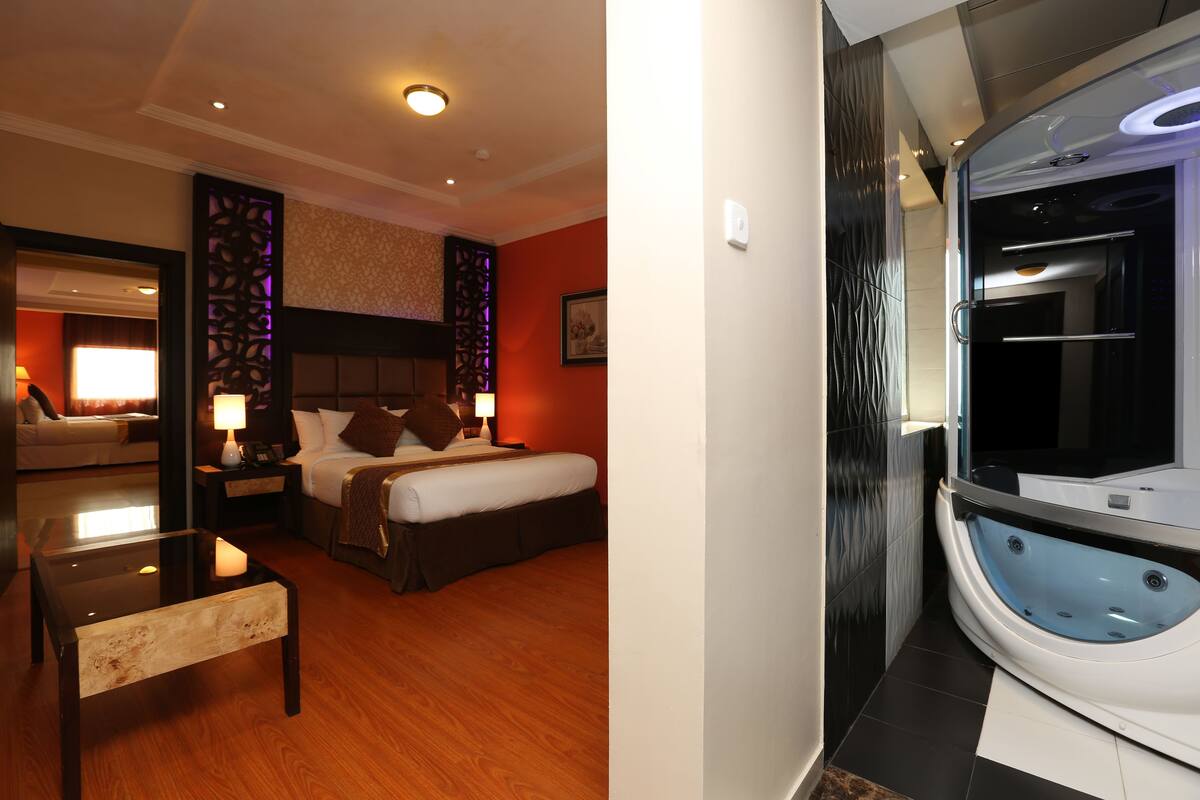 A hotel room with a bed, bedside table, and a large bathtub.