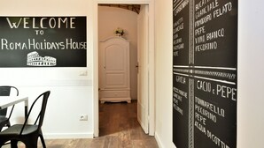 A hallway with a sign reading "Welcome to Roma Holidays House" and a chalkboard menu listing dishes like Carbonara, Amatriciana, and Cacio e Pepe. - Coliseum Suite (Rome)