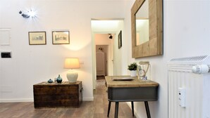 A hallway with a wooden floor, a small table with a lamp, a mirror, and framed pictures on the wall. - Coliseum Suite (Rome)