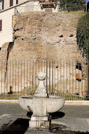 A stone fountain with a spout, surrounded by a metal fence, in front of a stone wall. - Coliseum Suite (Rome)