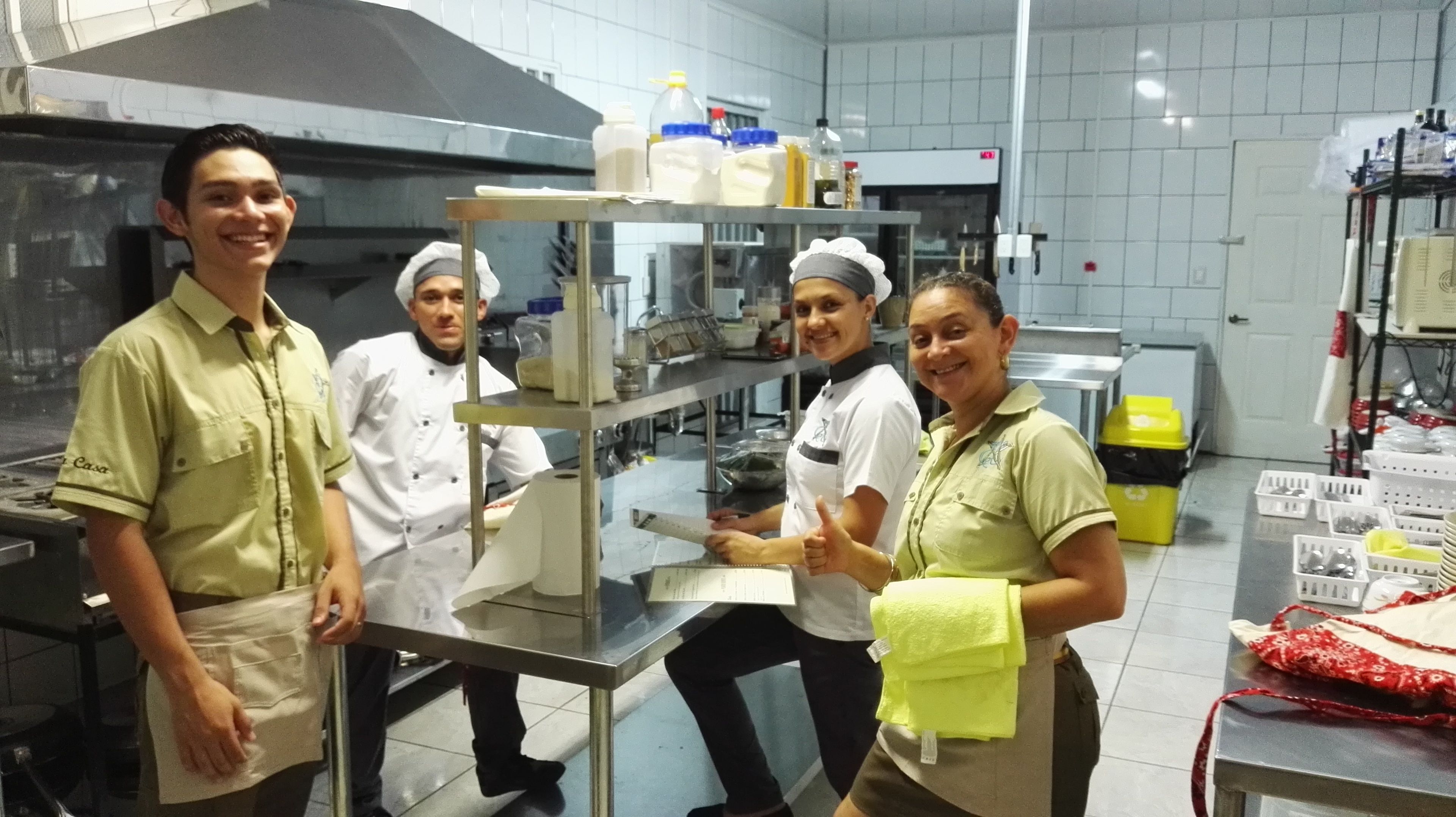 Um grupo de pessoas em uma cozinha com eletrodomésticos de aço inoxidável e prateleiras repletas de alimentos.