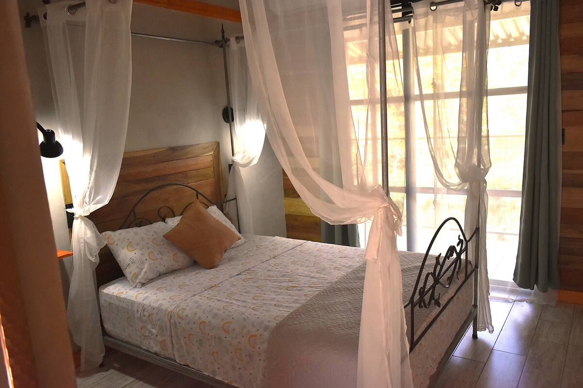 A bed with a canopy, a wooden headboard, and a window with curtains.