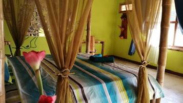 Una habitación con una cama cubierta por una colcha a rayas, un dosel con cortinas atadas en las esquinas y una pared verde con una ventana.