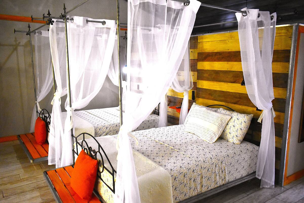 A room with two beds, each with a canopy, wooden slat headboard, and a patterned bedspread.