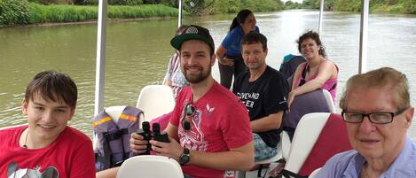 A group of people on a boat with a canopy overhead, surrounded by water and greenery.