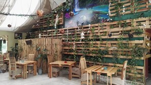 Un interior rústico con mesas y sillas de madera, un muro de bambú y un mural con paisaje forestal.