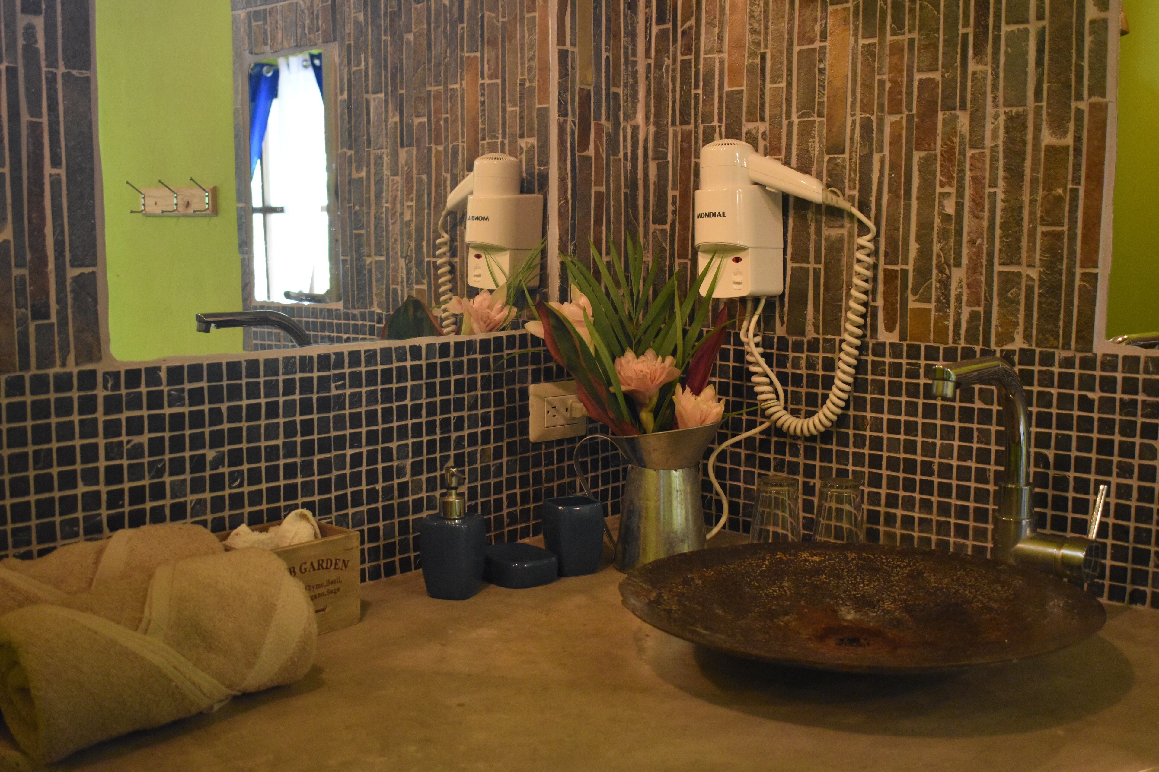 A bathroom with a tiled backsplash, a sink, a mirror, and two hair dryers mounted on the wall.
