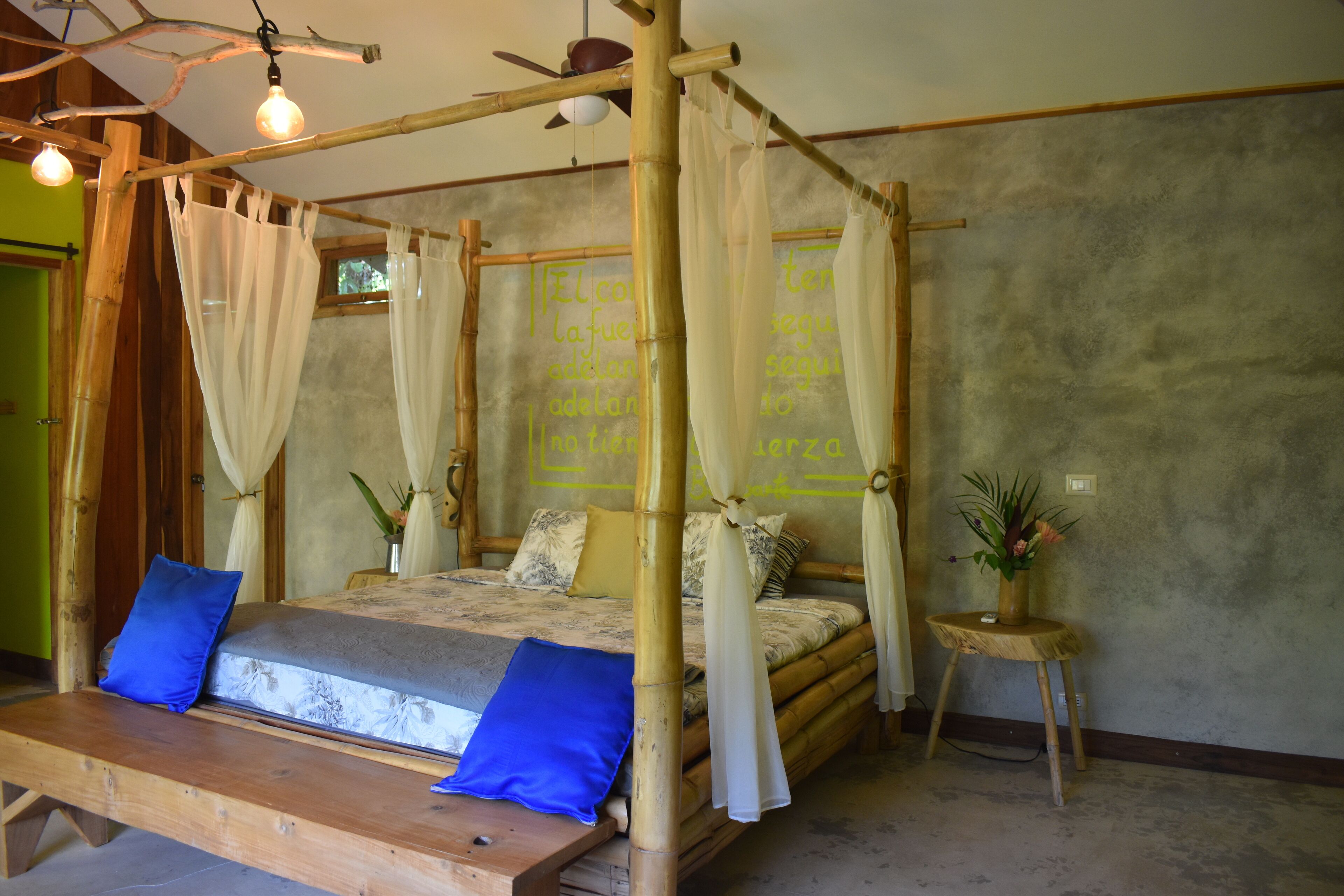 Una habitación con una cama con dosel, un banco de madera y una pequeña mesa con una planta.