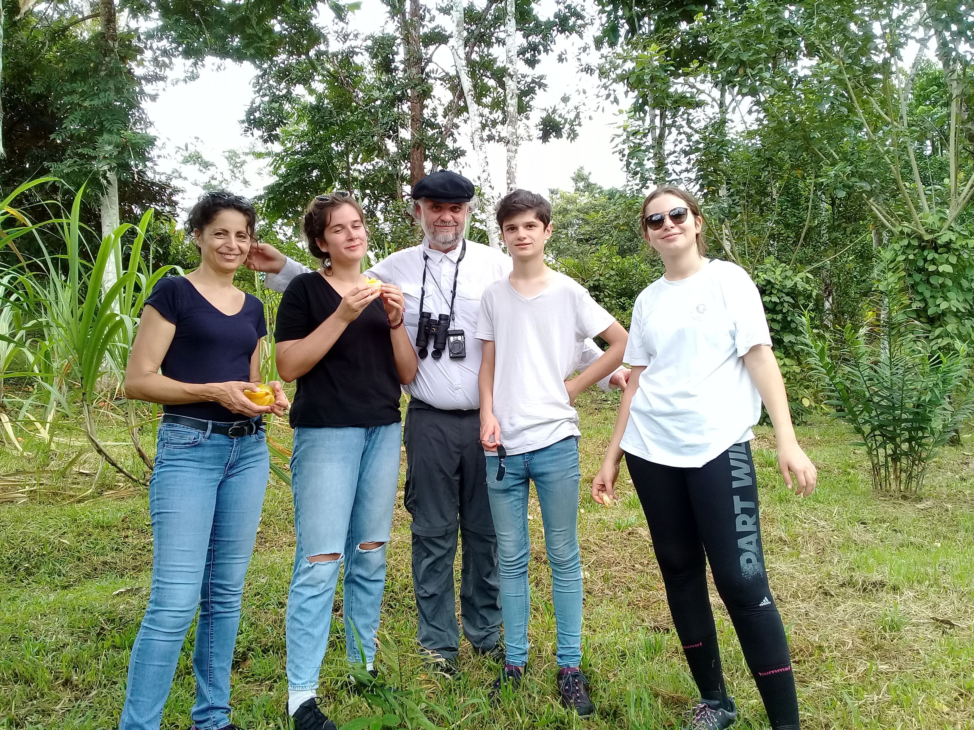 A group of people standing outdoors in a natural setting with trees and grass.
