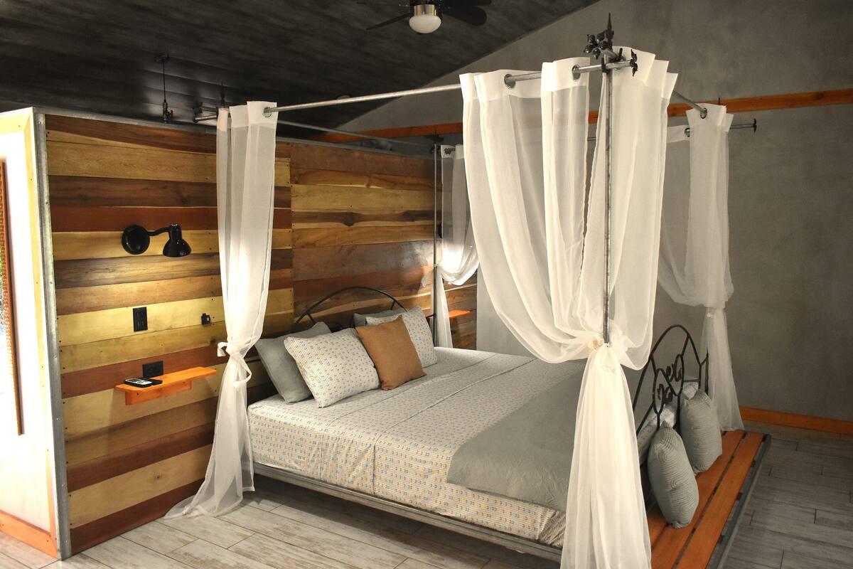 A bed with a canopy, wooden wall paneling, a bedside table, and a nightstand.