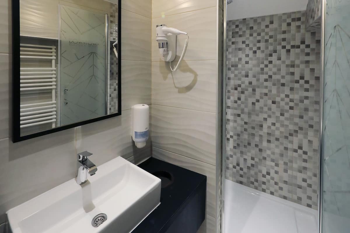 Ein modernes Badezimmer mit großem Spiegel, Waschbecken, Dusche mit Glastür und Handtrockner.