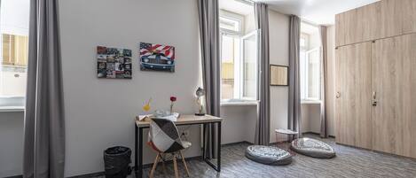 Une chambre moderne équipée d’un bureau, d’une chaise et de deux poufs. On y trouve également une grande armoire et une fenêtre avec des rideaux.