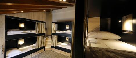 Une chambre avec des lits superposés, des poutres en bois et un petit bureau avec une lampe.