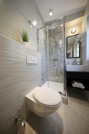 A modern bathroom with a glass-enclosed shower, a white toilet, and a sink with a mirror.