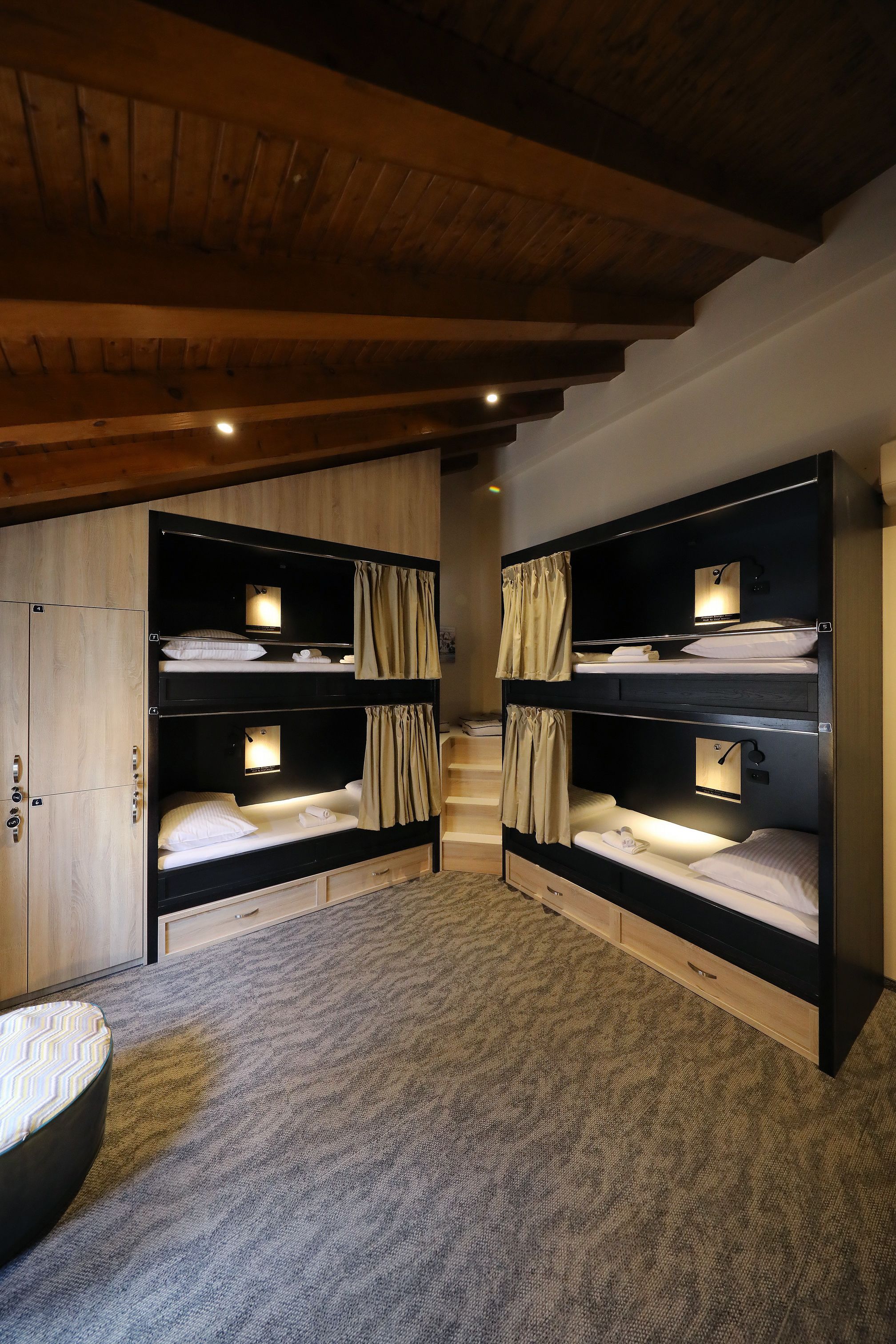 A room with bunk beds, wooden ceiling beams, and a carpeted floor.