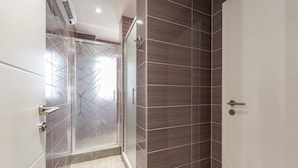 Un baño moderno con cabina de ducha de vidrio, suelo de baldosas y una puerta con manija.