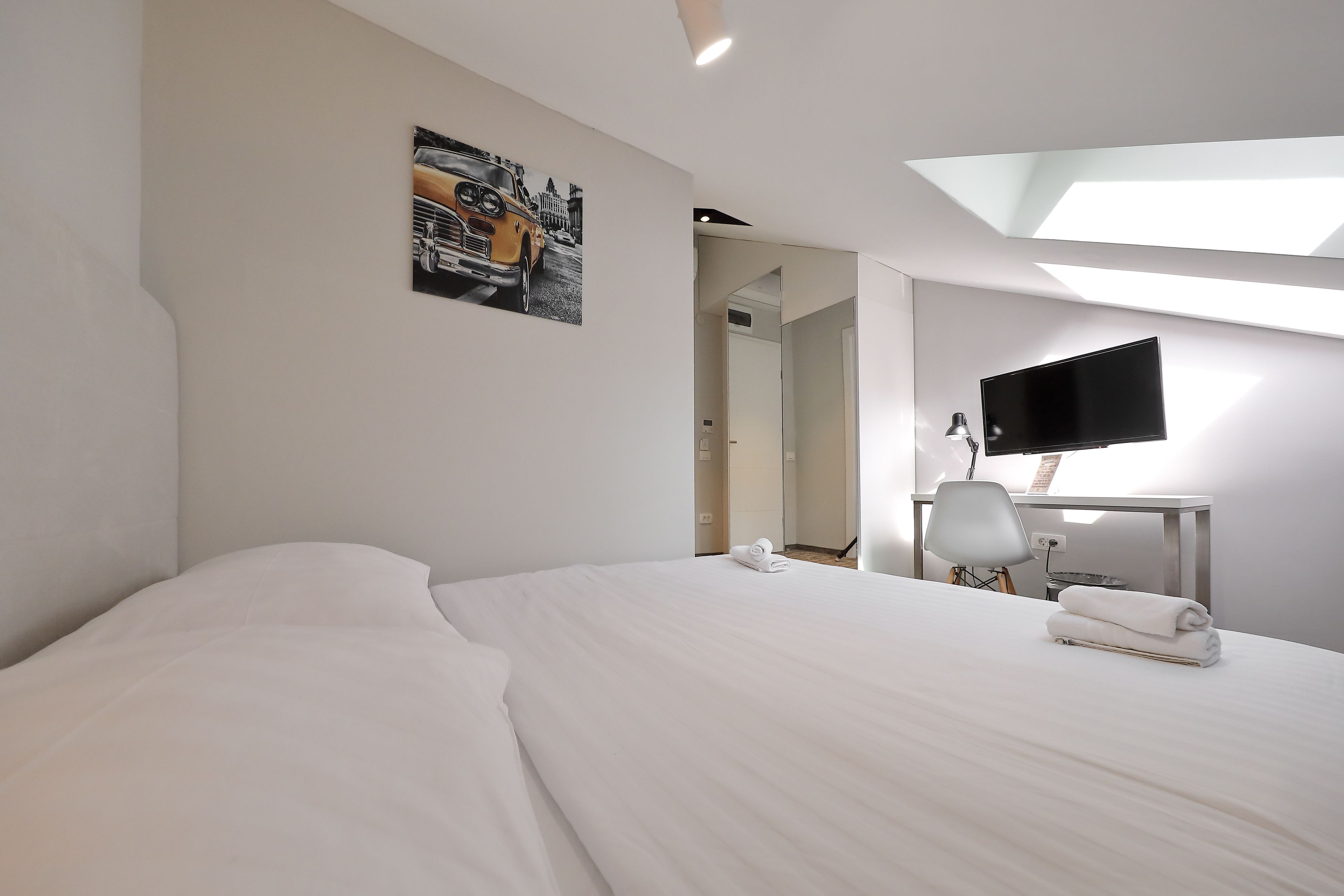 A hotel room with a large bed, a flat-screen TV, a desk with a lamp, and a painting on the wall.