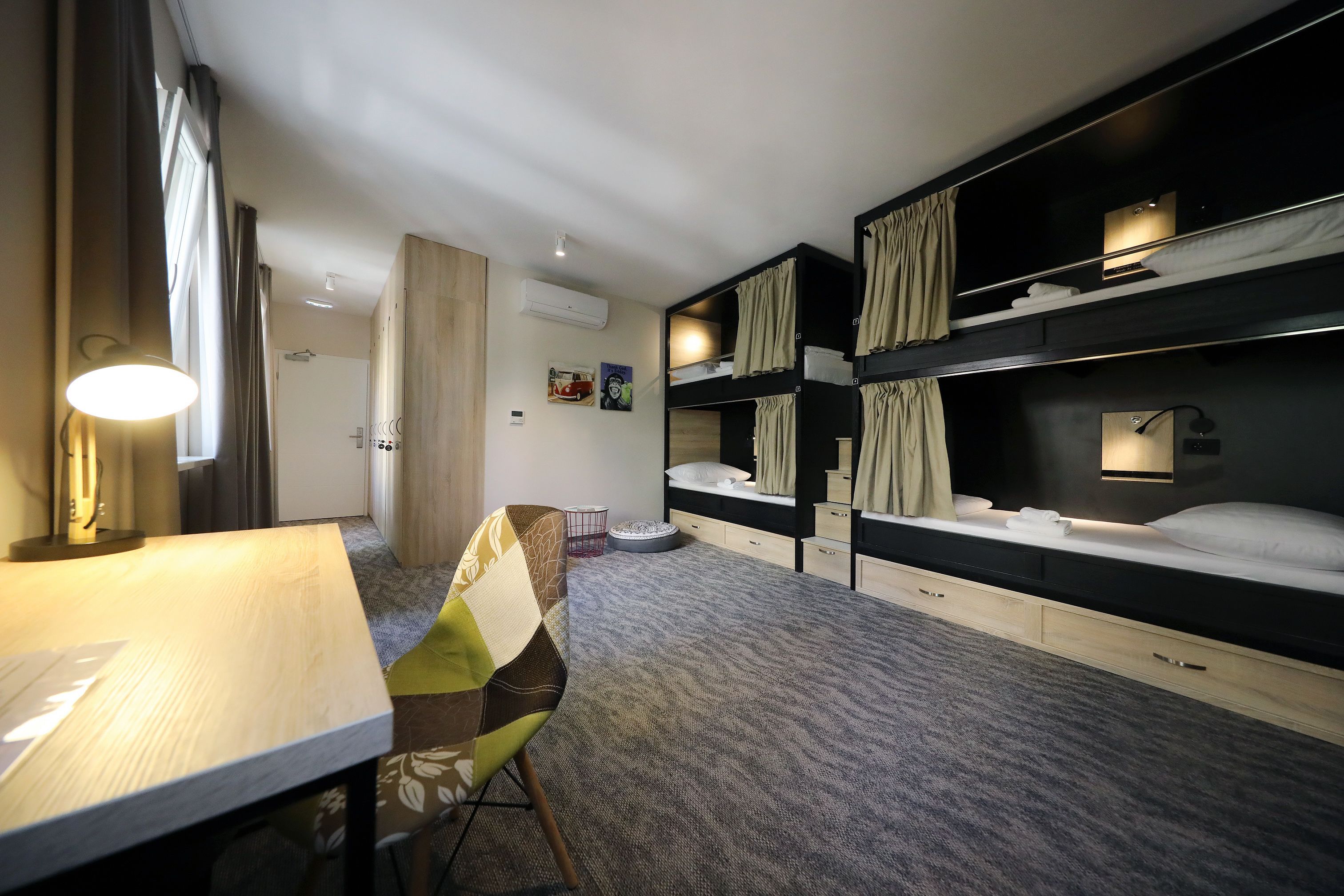 A hotel room with bunk beds, a desk, a chair, and a lamp.