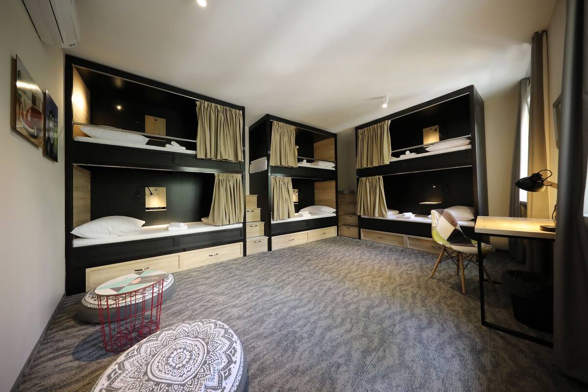 Ein modernes Hotelzimmer mit Etagenbetten, einem Schreibtisch, einem Stuhl und einem kleinen runden Tisch.