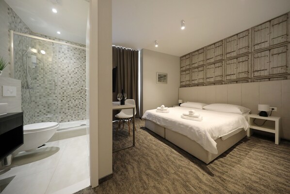 Habitación de hotel moderna con una cama grande, un escritorio, zona de ducha y baño.