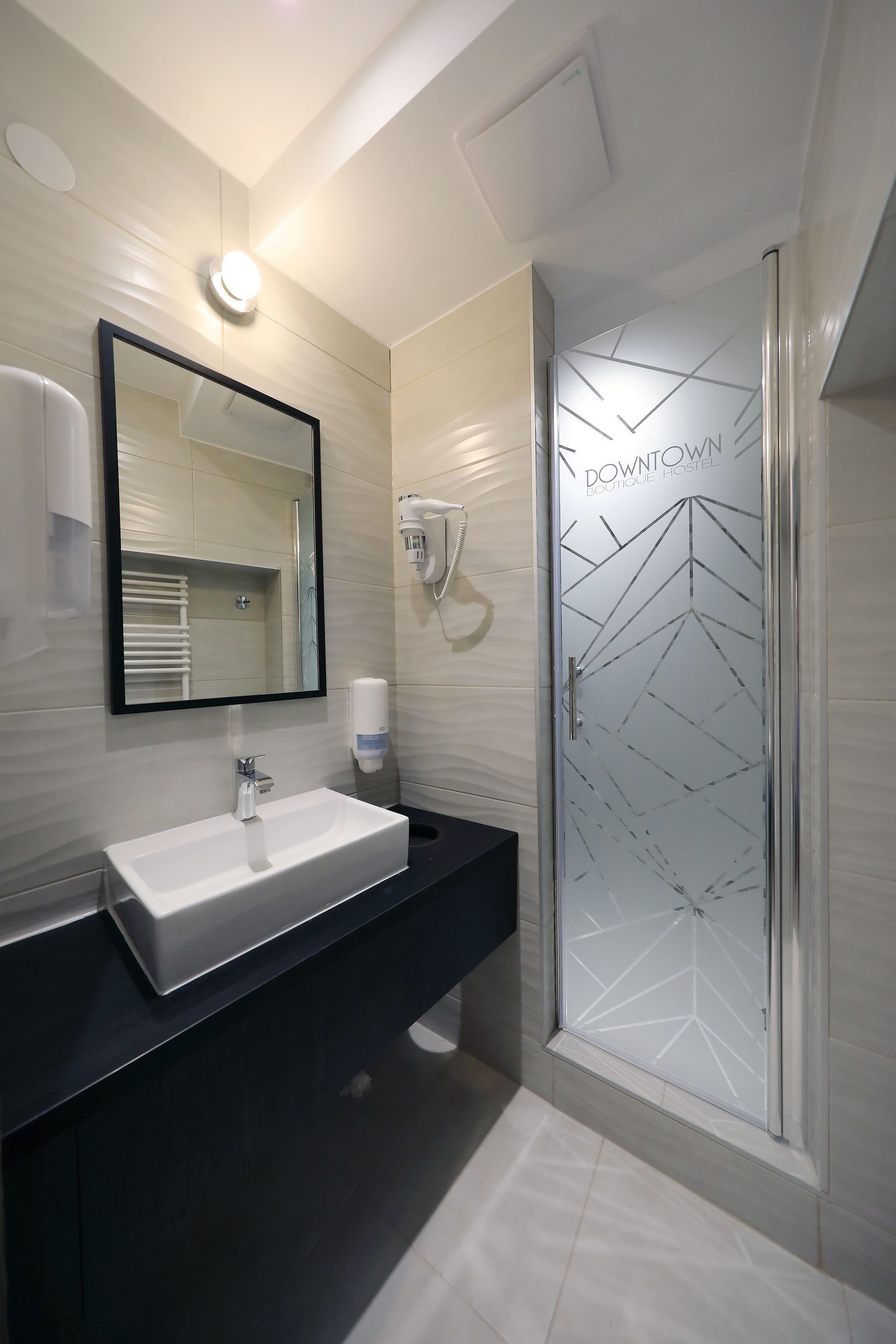 Een moderne badkamer met een witte wastafel, een grote spiegel en een douchecabine met een glazen deur en een geometrisch patroon.