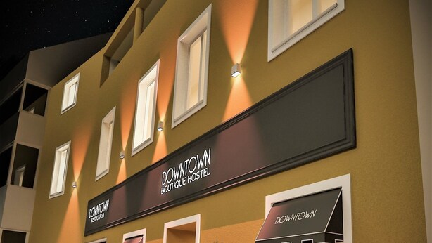 Un edificio con un letrero que dice "DOWNTOWN BOUTIQUE HOSTEL" y asientos exteriores con mesas y sillas.
