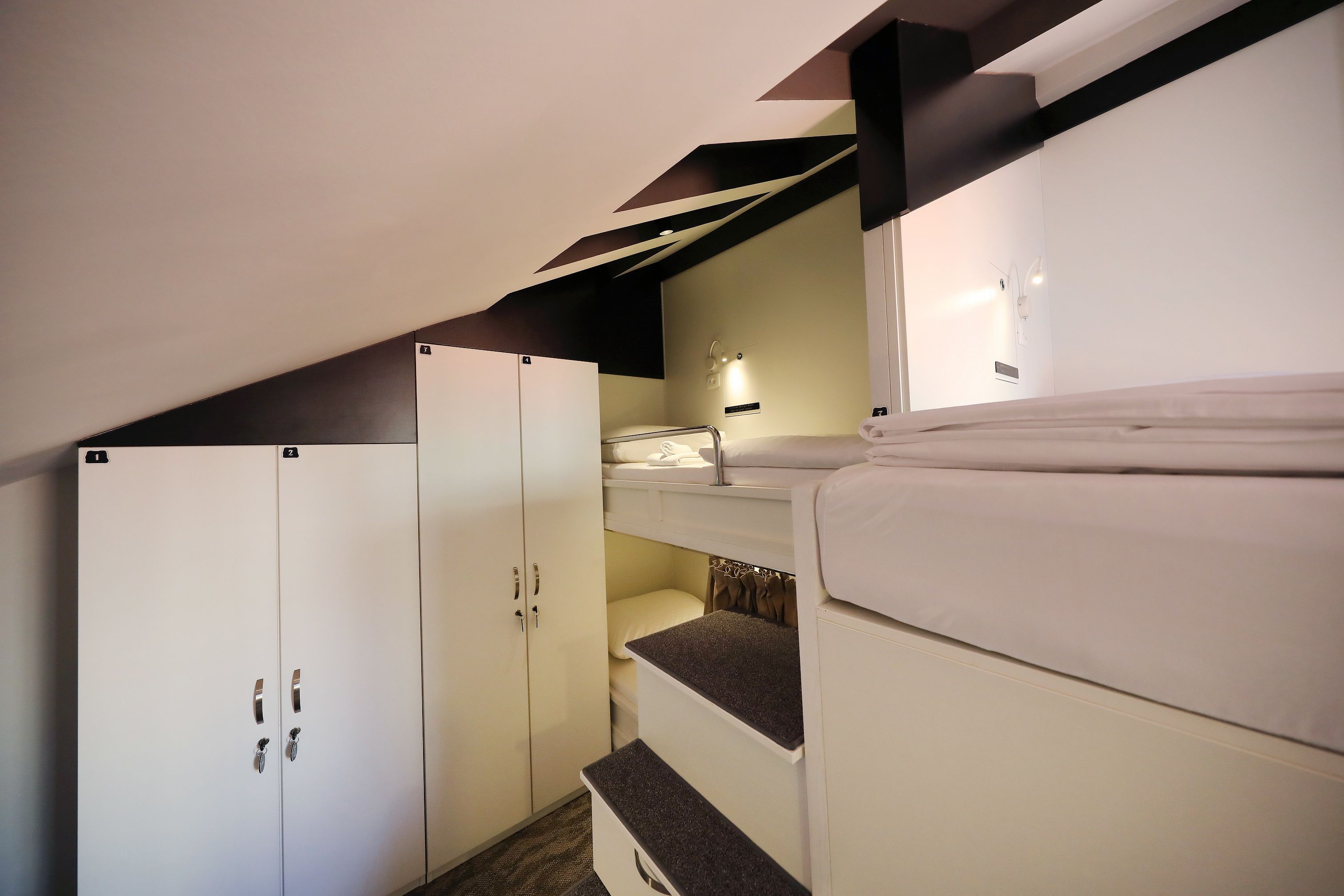 Habitación de hotel pequeña con literas, armario y un rincón de escritorio.