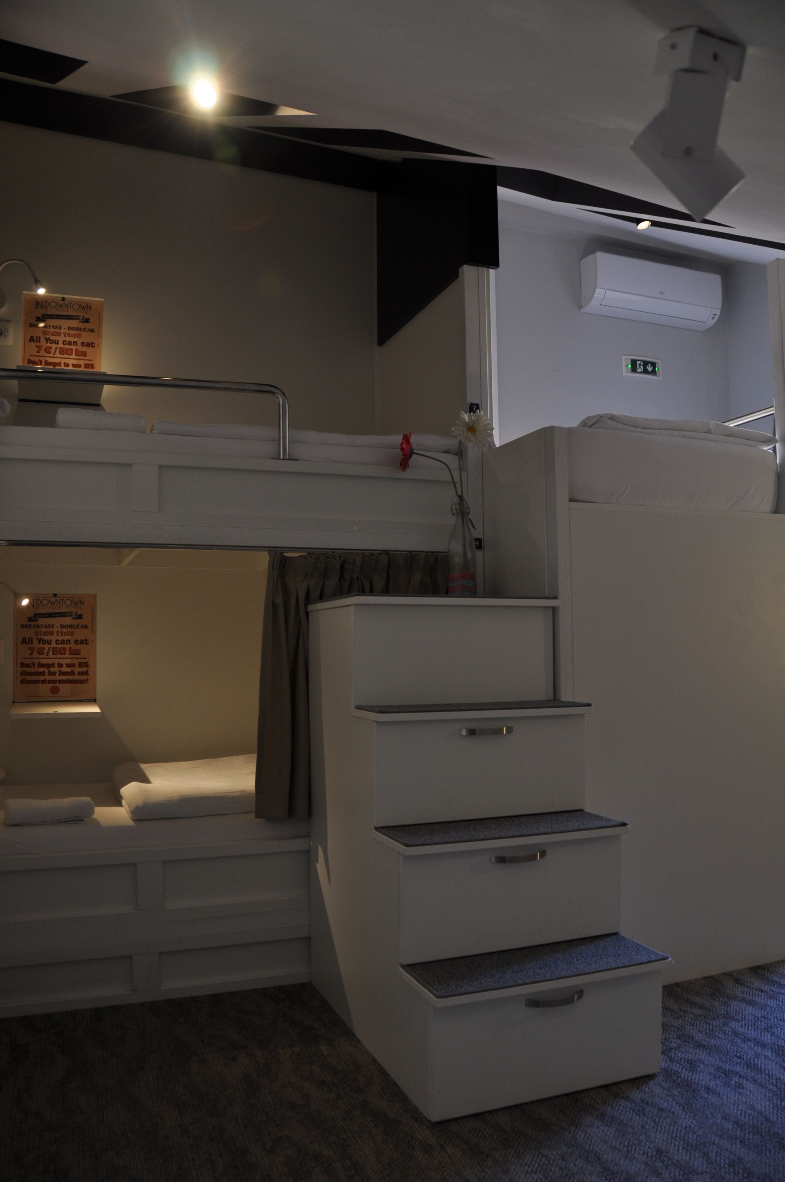 Una cama litera con un escritorio pequeño y cajones, un equipo de aire acondicionado y un letrero que indica la disponibilidad de desayuno.